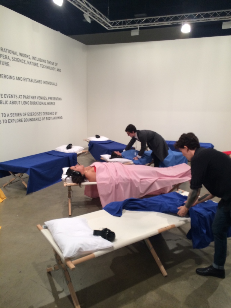 Facilitadores ajudam as pessoas a se deitarem na cama do "Sleeping Exercise", de Marina Abramovic, na Art Basel
