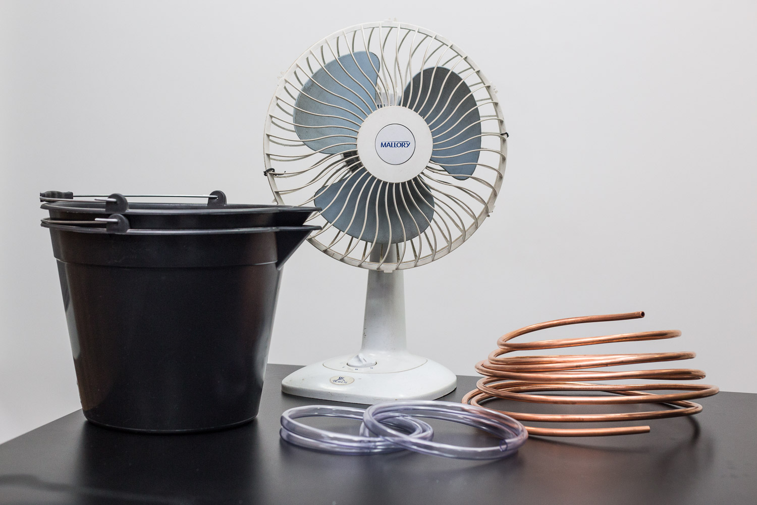 <strong>Nível de dificuldade: </strong> Seu Apelido É "McGyver"

Você vai precisar de:
- 1 ventilador - não pode ser daquele embutido.
- 2 baldes
- 7m de tubo flexível de cobre (difícil de achar, compramos pela internet e saiu muito mais barato)
- 1m de mangueira plástica, cortada em duas partes iguais.
- Silver tape
- Canivete para cortar a mangueira.