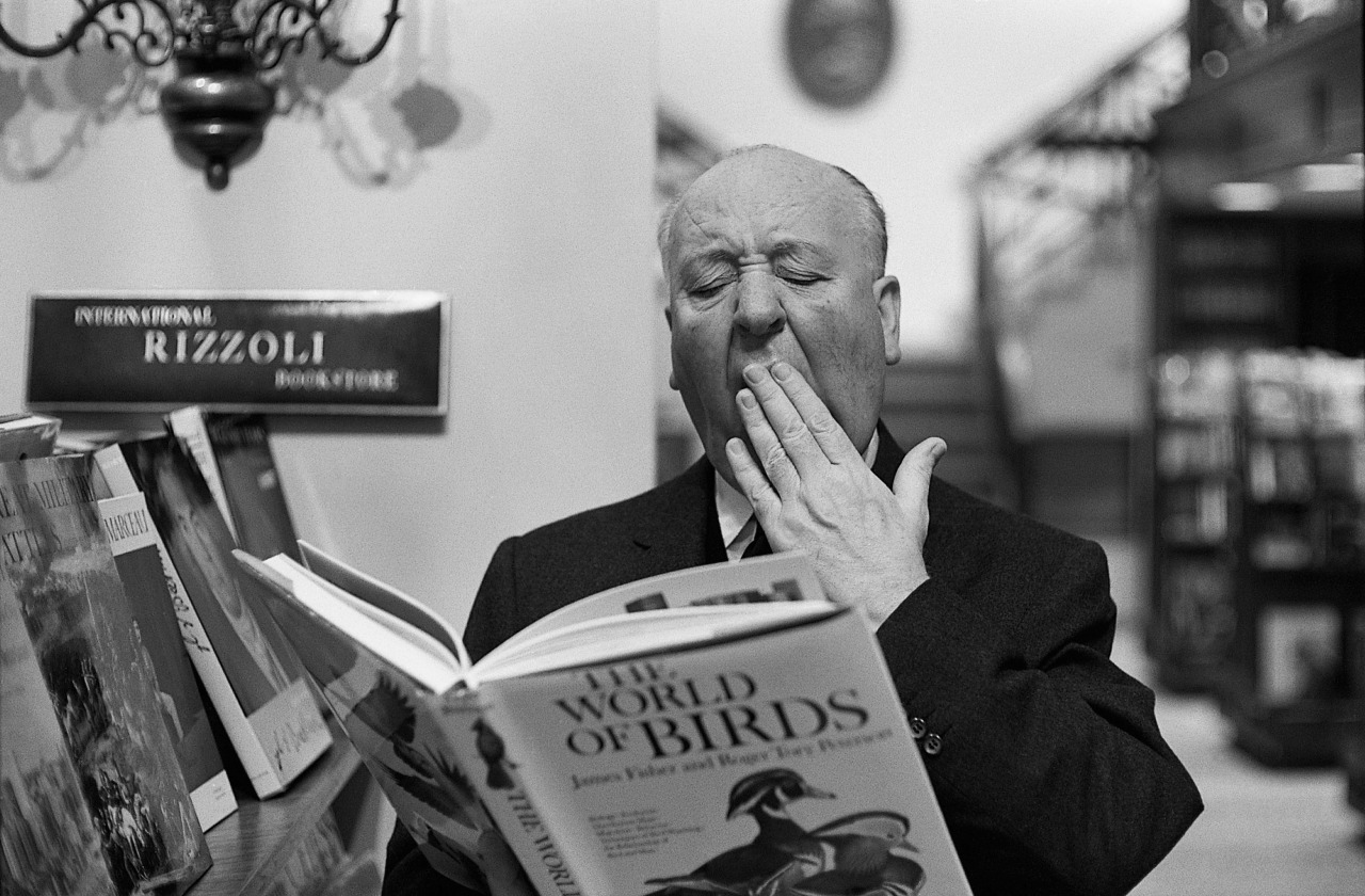O mestre do suspense brinca de bocejar lendo "The World of Birds", de James Fisher e Roger Tory Peterson, na época em que filmava "Os Pássaros" (1963)