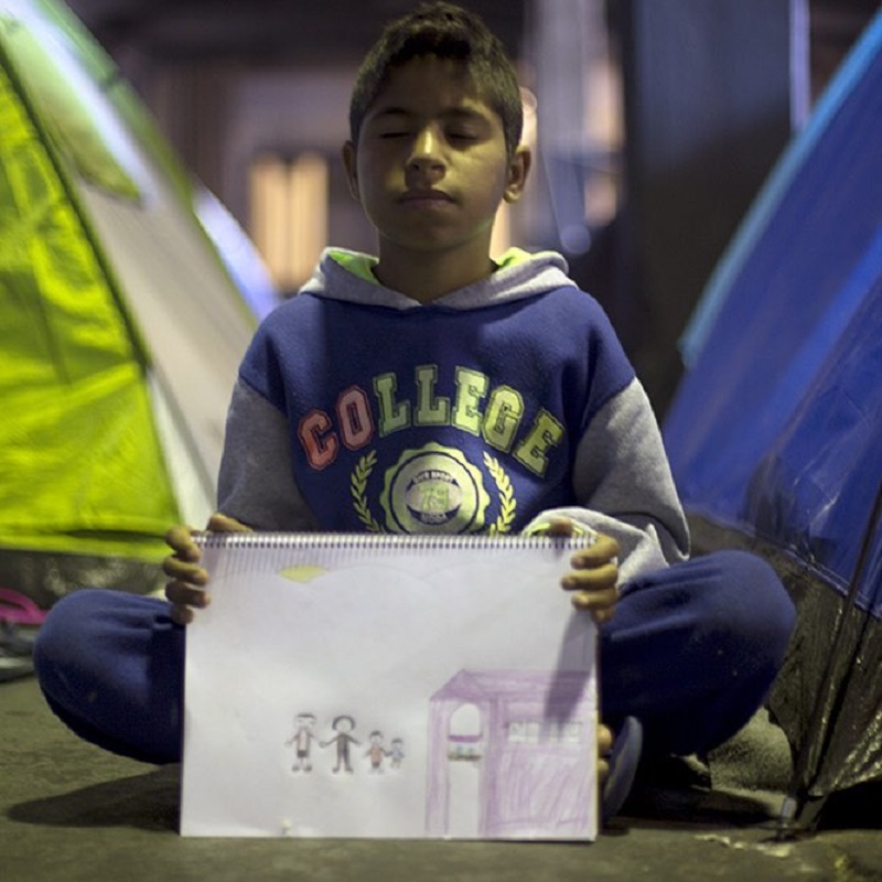 Na Grécia, o garoto sírio desenha a família, que está na Síria tentando fugir dos confrontos. Ele está sozinho.